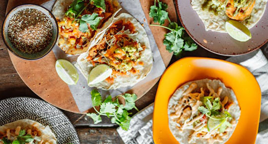 Assorted tacos with lime wedges, cilantro, and various fillings served on plates and a wooden board.