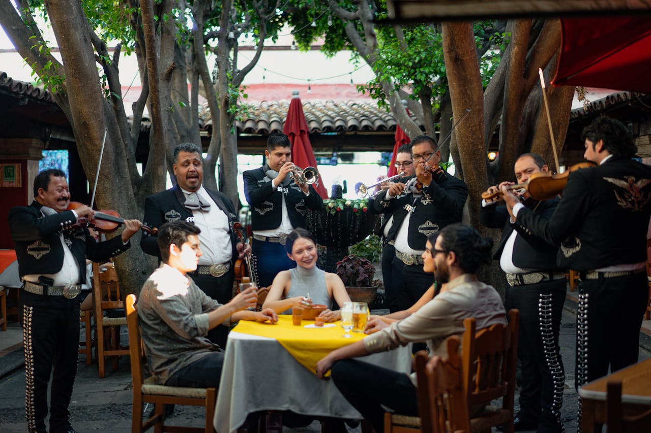 A group of people in traditional Mexican outfits seated around a table, engaged in conversation and enjoying their time together.